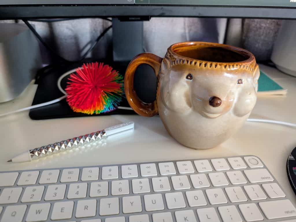 Colorful hedgehog mug on desk with keyboard and decorative spiky toy behind it. Everything I need for my ADHD brain dump session.