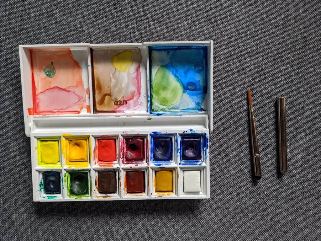 Vibrant watercolor paints palette with brushes on textured gray surface, perfect for artistic creativity.